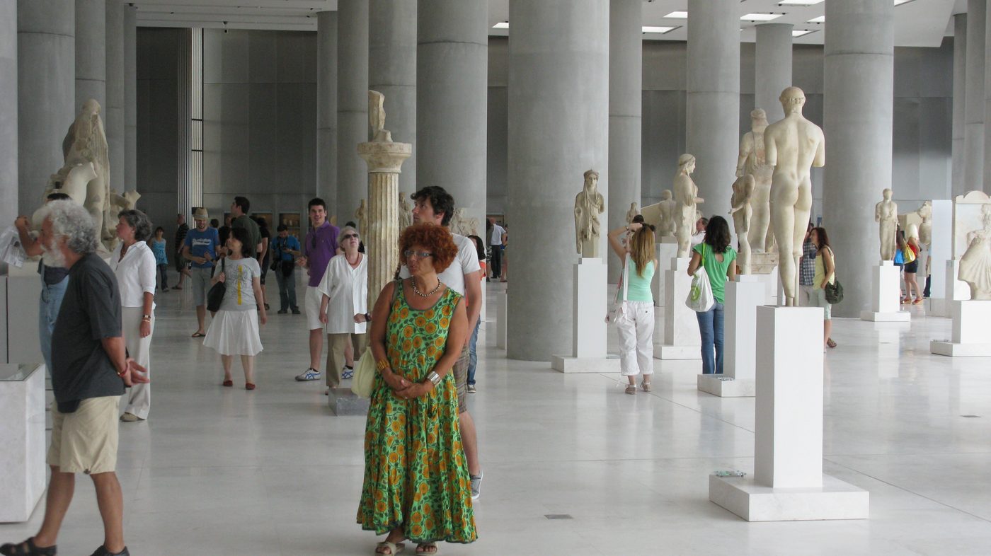 The bright, modern interior of the Acropolis Museum in Athens with ancient Greek statues and artifacts displayed in a spacious gallery
