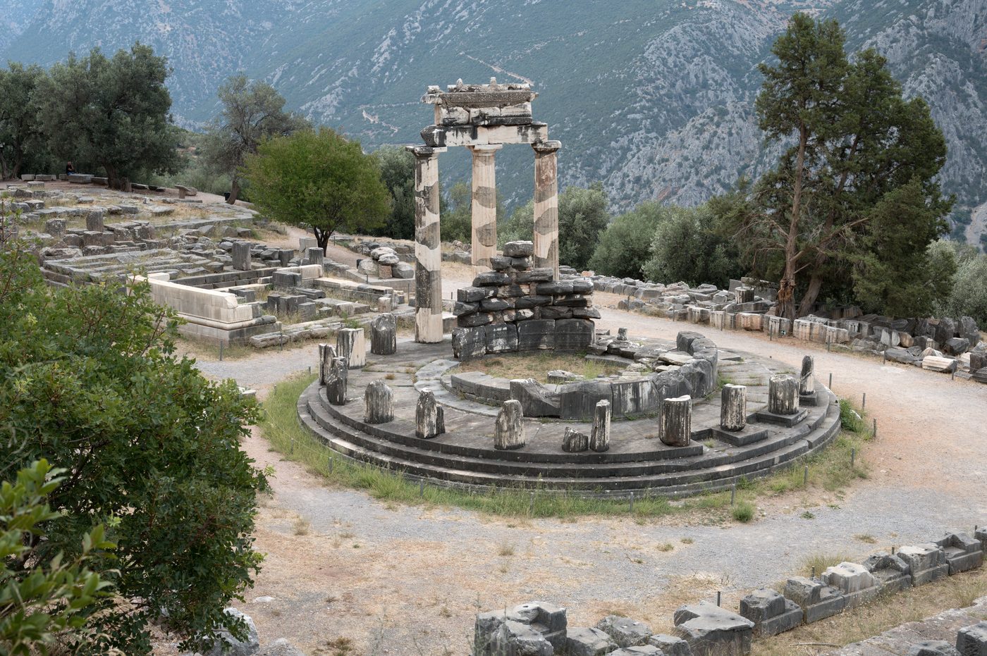 The Tholos circular temple at Delphi with three restored Doric columns against a mountain backdrop