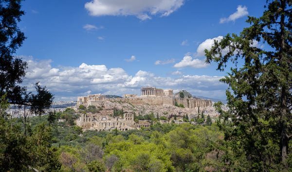 Panoramic view of the Acropolis and Parthenon from Filopappou Hill in Athens, with green trees in the foreground and blue sky above