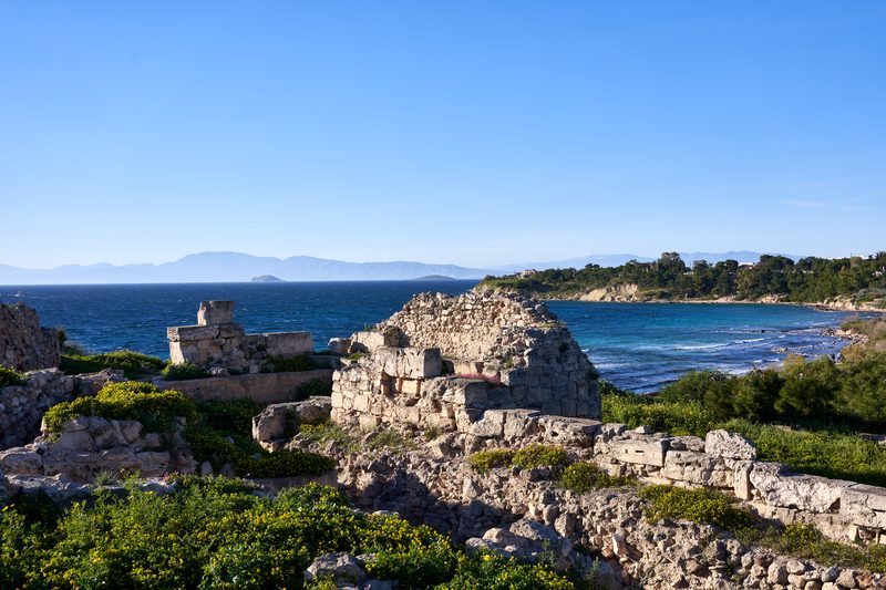 Ancient ruins at the Kolona archaeological site on Aegina island with Kolona beach and the Peloponnese coastline visible in the background