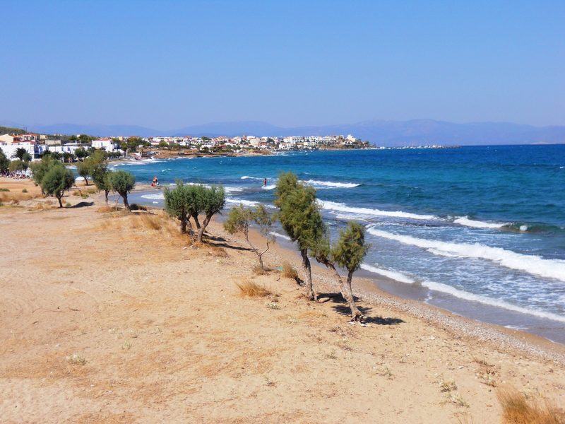 View along the northern beach at Skala on Agistri island, with turquoise water and the village of Megalochori in the distance