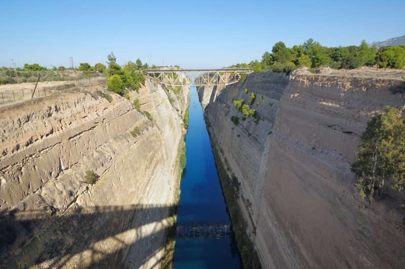 Aerial view of the Corinth Canal cutting through solid rock, with steep limestone walls dropping to the narrow waterway below