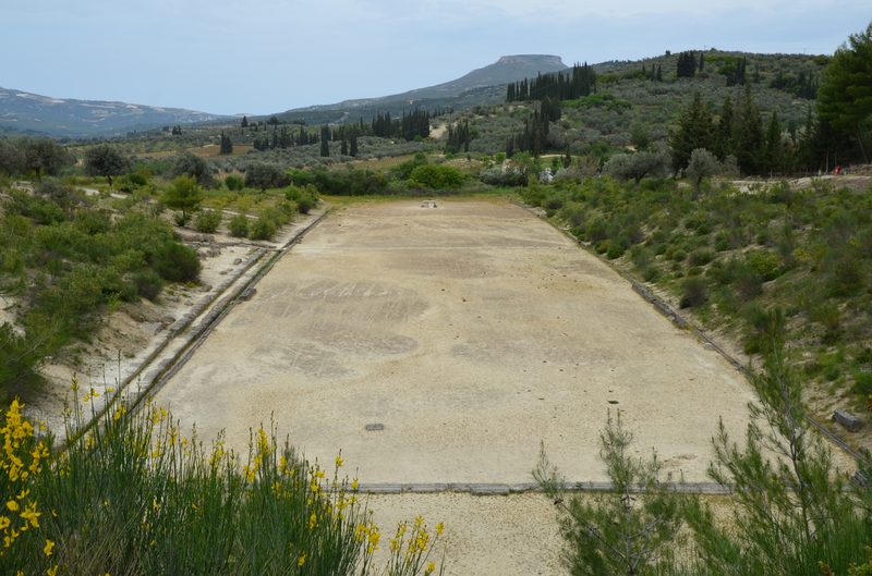 The ancient stadium of Nemea showing the stone starting blocks in the foreground and the long racing track stretching into the distance between grassy slopes