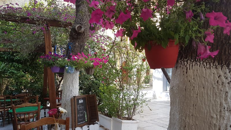 A shaded taverna courtyard in Plaka with hanging flowers and outdoor tables set for lunch