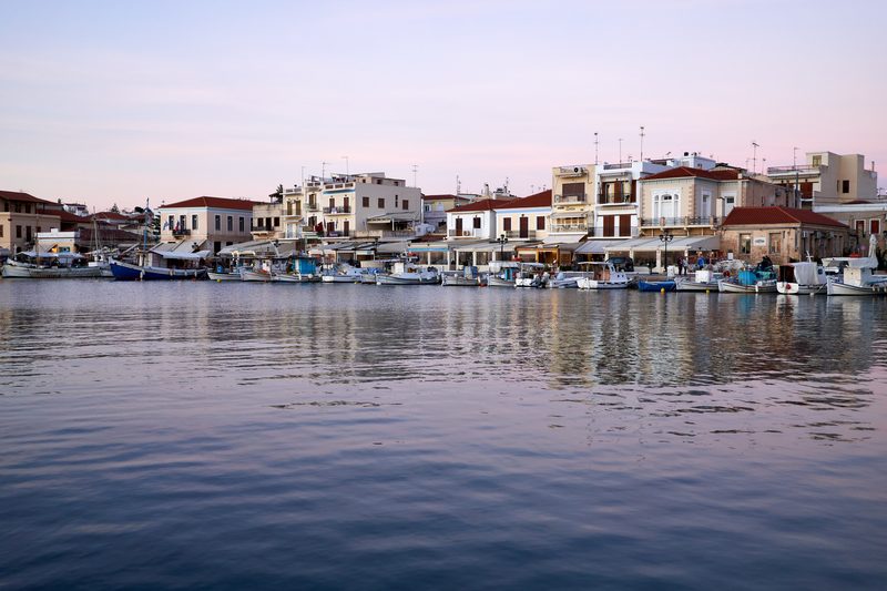 Aegina harbour waterfront in the evening with boats and traditional buildings along the promenade