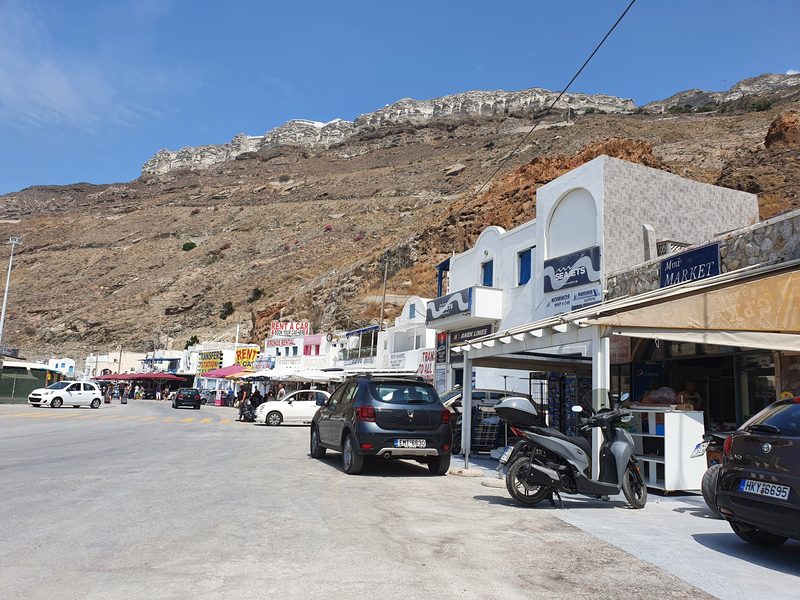 Ferry company offices and car rental booths lining the road at Santorini's Athinios port