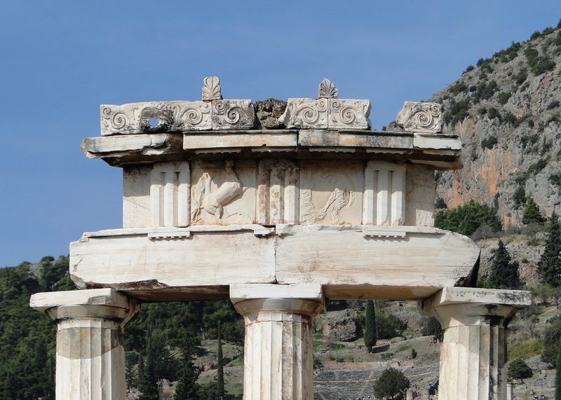 The Tholos circular temple at Delphi with three restored Doric columns against a mountainous Greek landscape