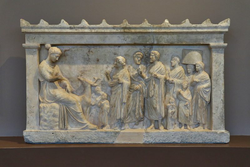 Ancient marble votive relief showing a family bringing a goat to sacrifice before the seated goddess Artemis at Brauron