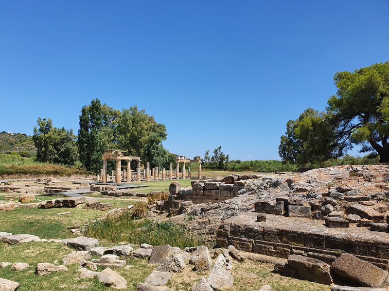 Low ruined foundations at Brauron with the restored stoa colonnade visible in the background