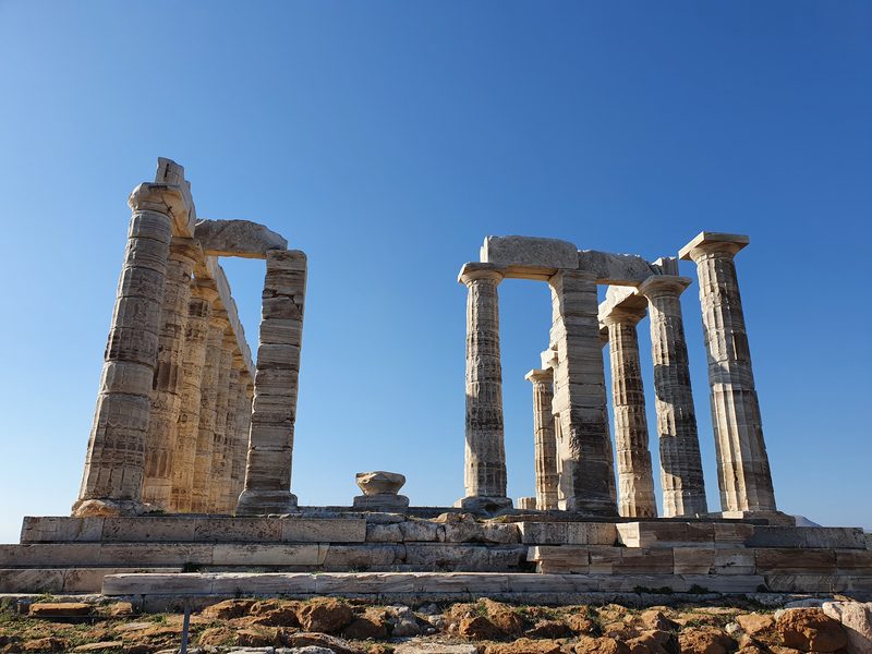 A low-angle view of the Temple of Poseidon showing its two surviving groups of columns in bright sunlight