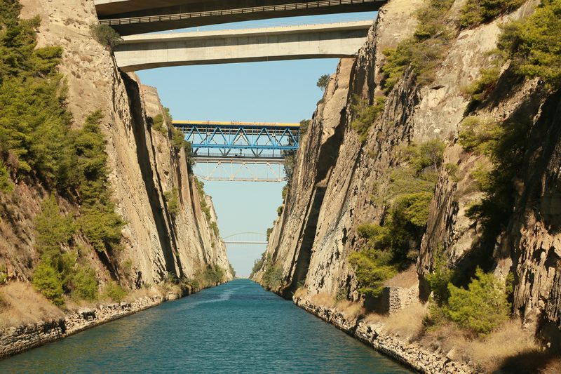 The Corinth Canal viewed from above, with steep vertical rock walls on both sides and calm blue water far below