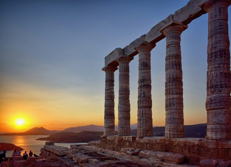 Marble columns of the Temple of Poseidon standing on the clifftop at Cape Sounion against the evening sky over the Aegean Sea