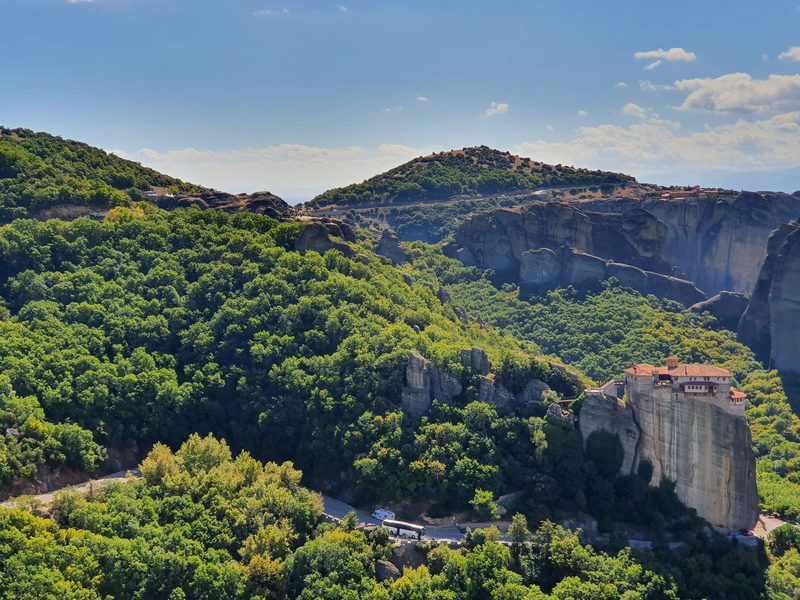 The road winding between the Meteora rock pillars, with a tour bus parked below a clifftop monastery