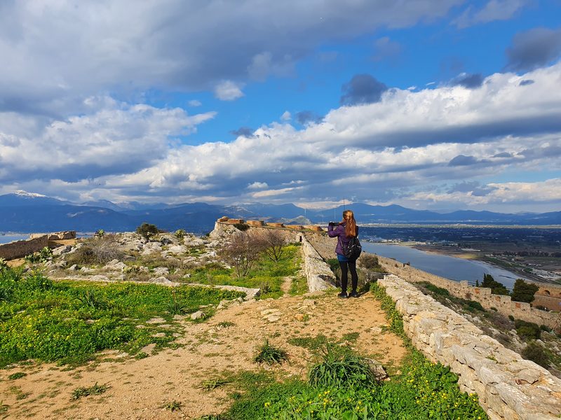 A visitor at the ramparts of Palamidi fortress looking out over the Argolic Gulf toward snow-capped mountains