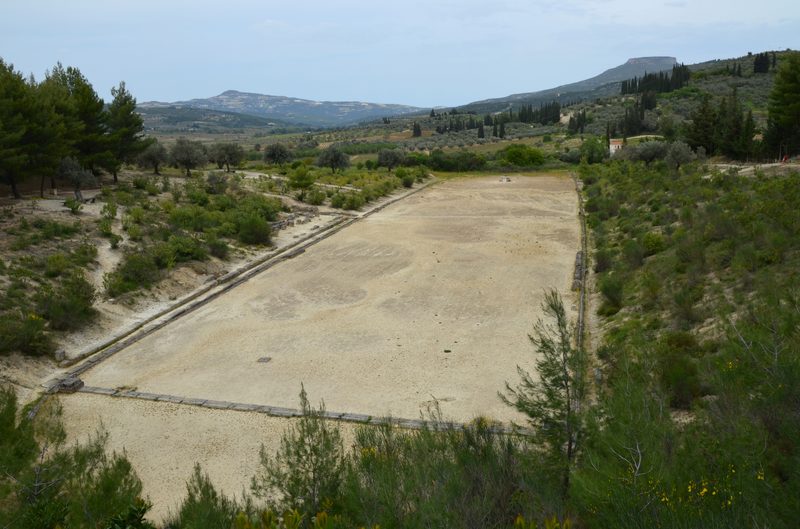 The ancient stadium at Nemea, a long grassy track flanked by earthen embankments with hills in the background