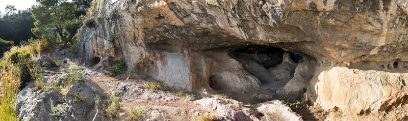 The Cave of Euripides on a hillside on Salamis island, a wide panoramic view showing the rocky cave entrance overlooking the Saronic Gulf