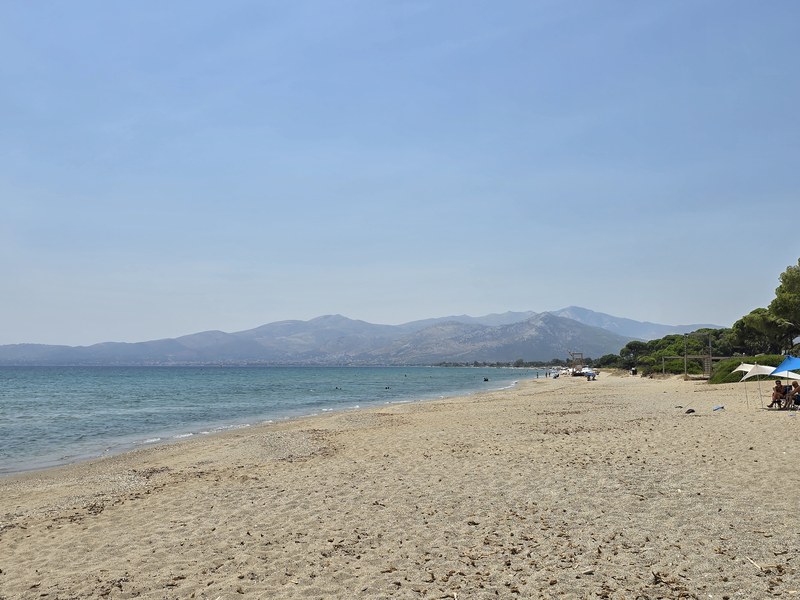 Sandy beach at Schinias with beach umbrellas and mountain views across the bay near Marathon
