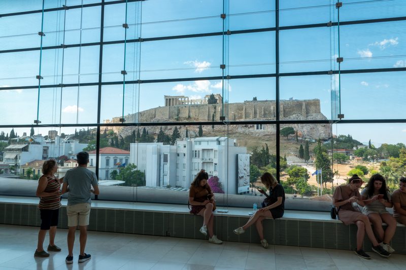 Interior of the Acropolis Museum Parthenon Gallery with glass walls framing a view of the Parthenon on the hill above