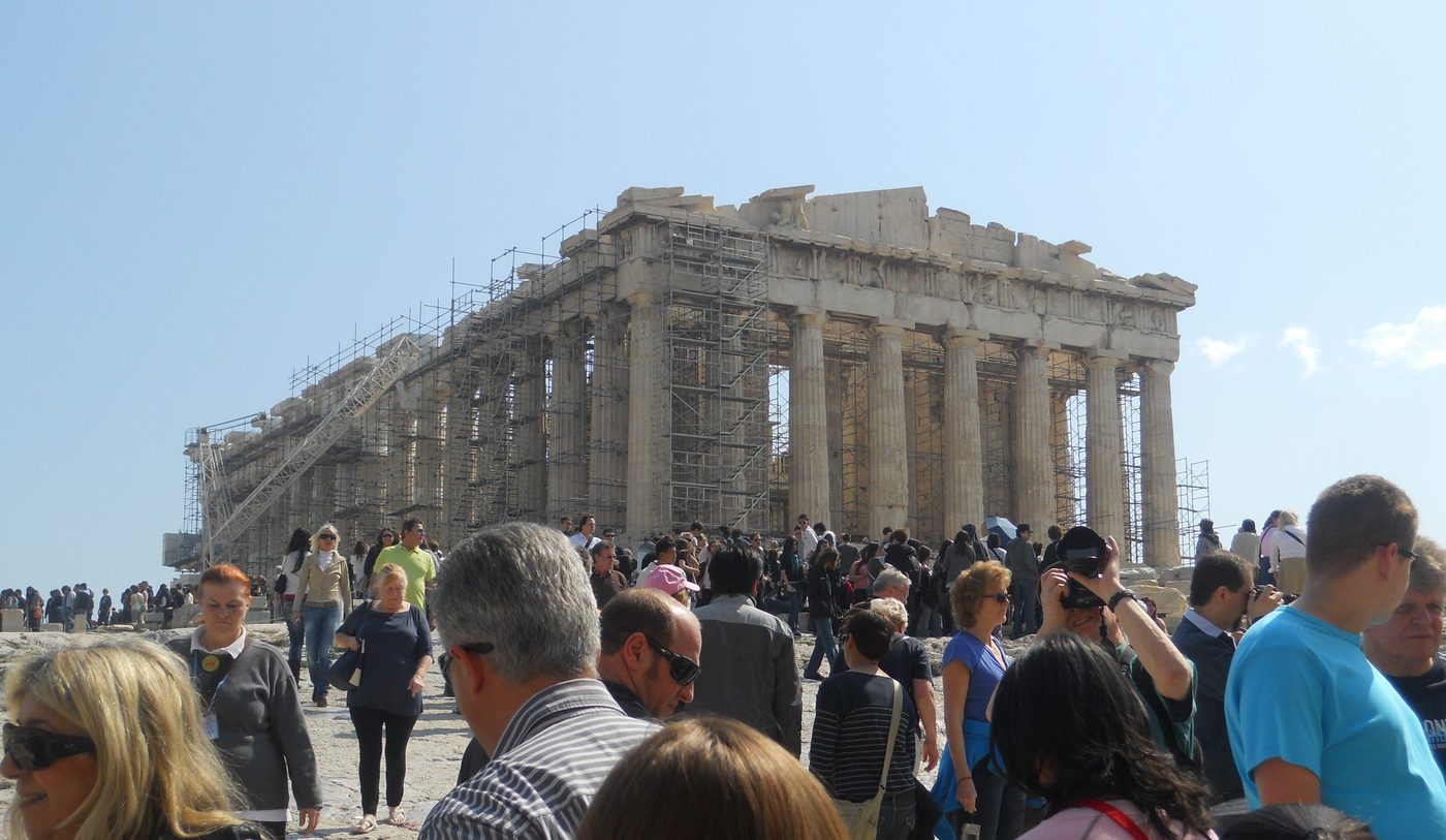 Tourists walking along the marble pathways of the Acropolis with the Parthenon in the background on a sunny day in Athens